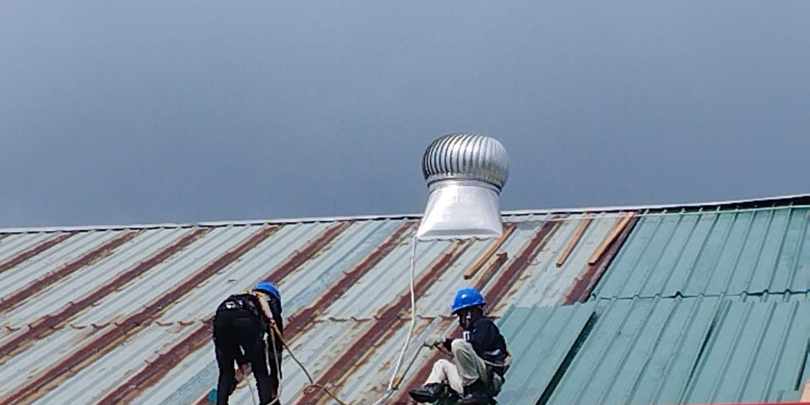 Teknisi berhelm memperbaiki atap gudang dengan ventilator turbin